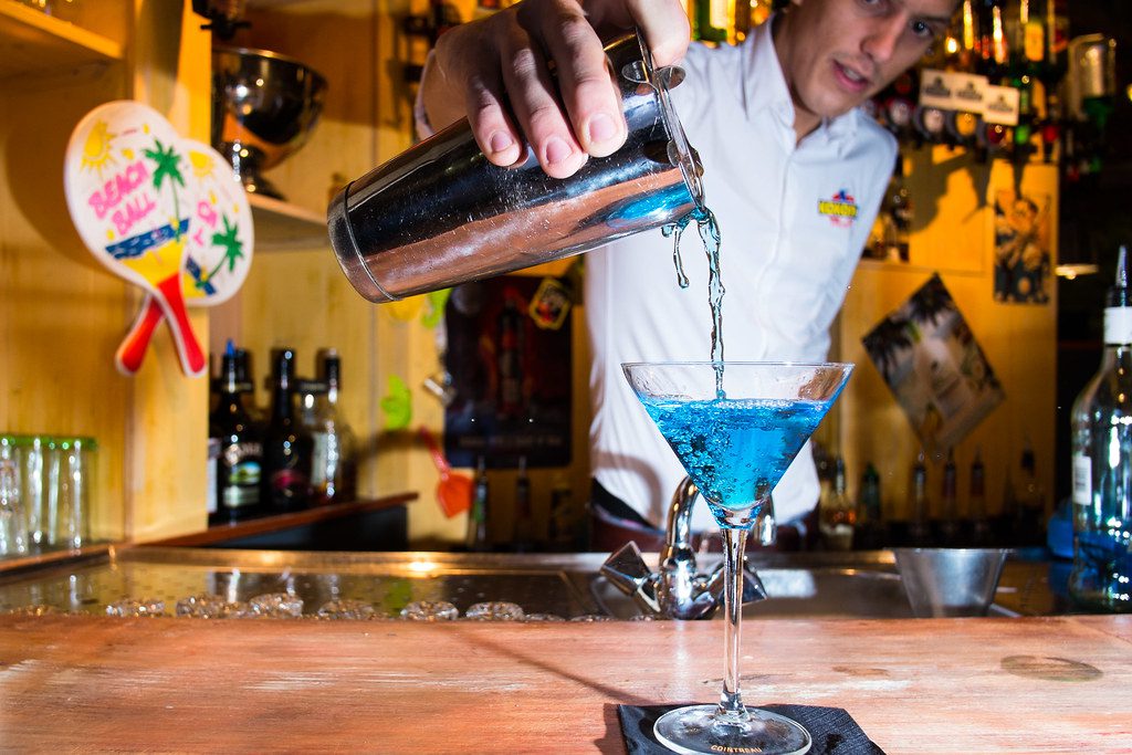 Bartender pouring cocktail from a shaker into a martini glass at a bar